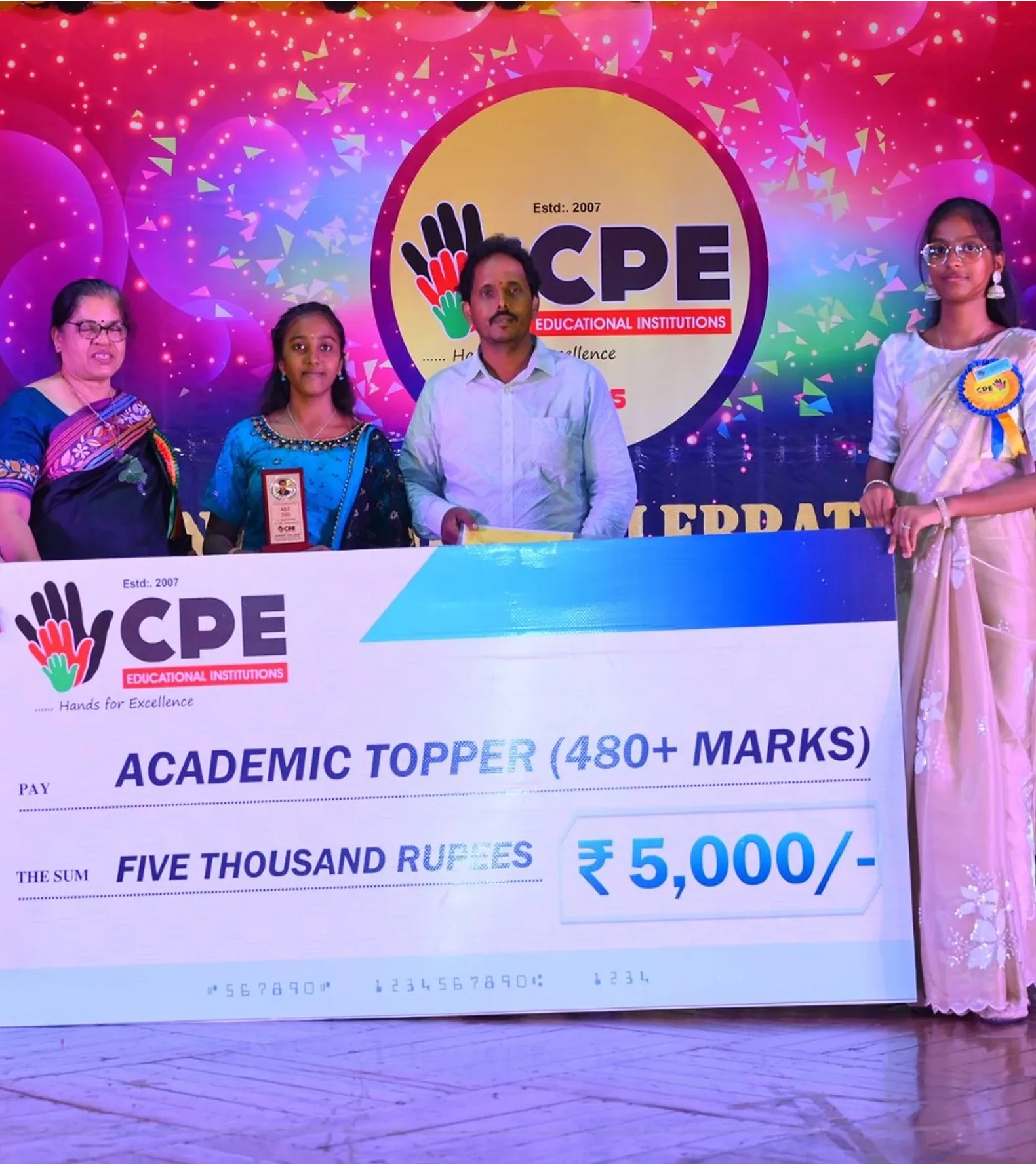 An academic topper receiving a ₹5,000 cheque for scoring over 480 marks